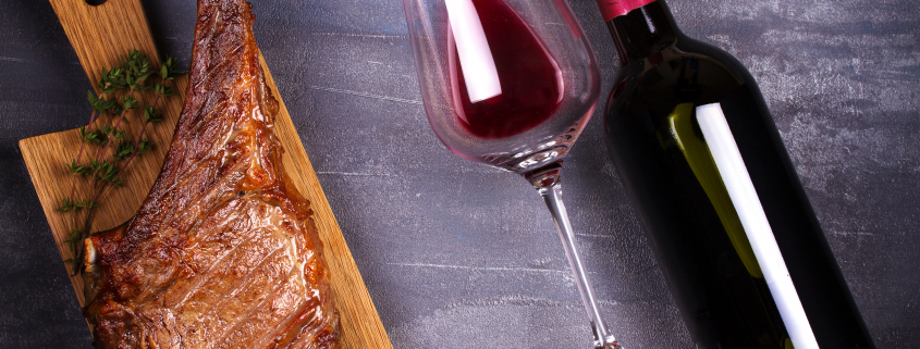 steak on a cutting board beside wine glass and wine bottle