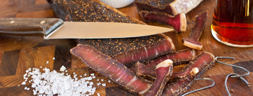 Biltong in South Africa as part of the country's culinary tradition, using good quality beef or game, coarse salt, ground spices and vinegar, and air dry the meat using wire hooks.