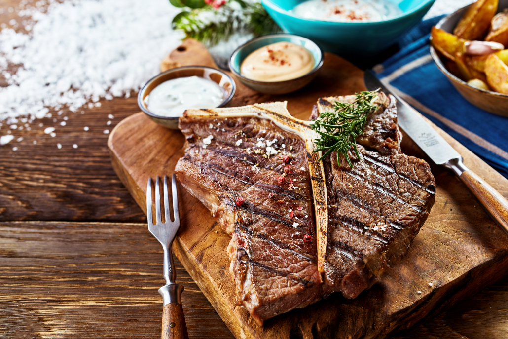 Piece of grilled t-bone steak on wooden cutting board with side dishes in close up view