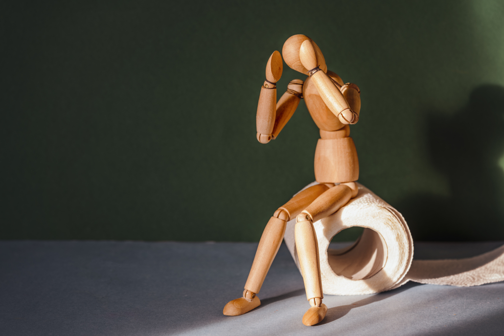 Wooden figure sit on a roll of toilet paper. Concept of the problem with digestion.