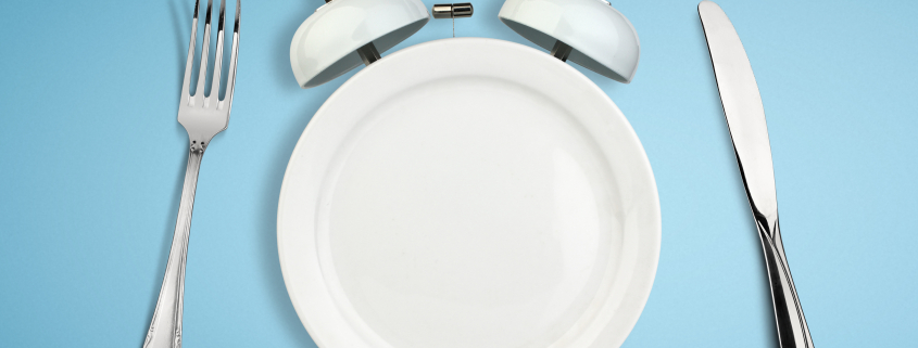 Concept of intermittent fasting, diet and weight loss. Plate as Alarm clock on blue