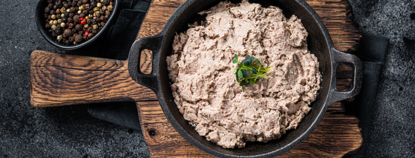Duck pate Rillettes de Canard in a pan with greens. Black background. Top View.