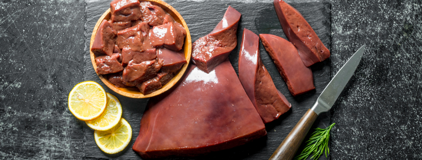 Sliced raw liver on a stone Board and on a plate. On dark rustic background