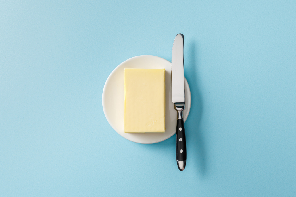 top view of butter and knife on white plate on blue background