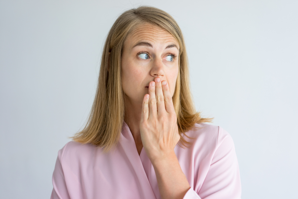 Portrait of shocked young Caucasian woman wearing pink blouse covering mouth with hand. Fear, bad breath concept