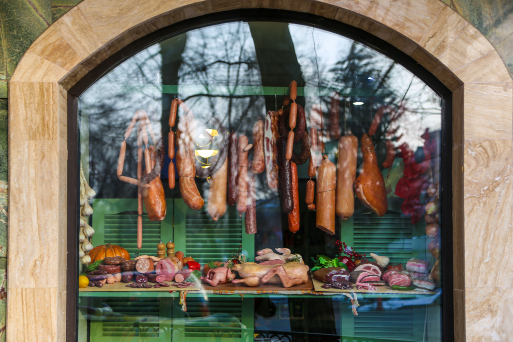 Colorful butcher shop display showing various meat behind a window with reflection