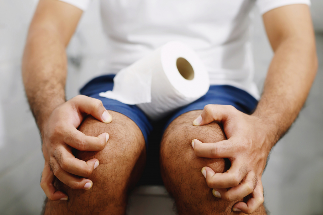 Man suffers from diarrhea hand hold tissue paper roll in front of toilet bowl. constipation in bathroom. Treatment stomach pain and Hygiene, health care