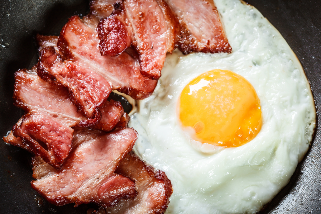 Slices of smoked bacon and fried egg in frying pan. Eating habits concept. Top view