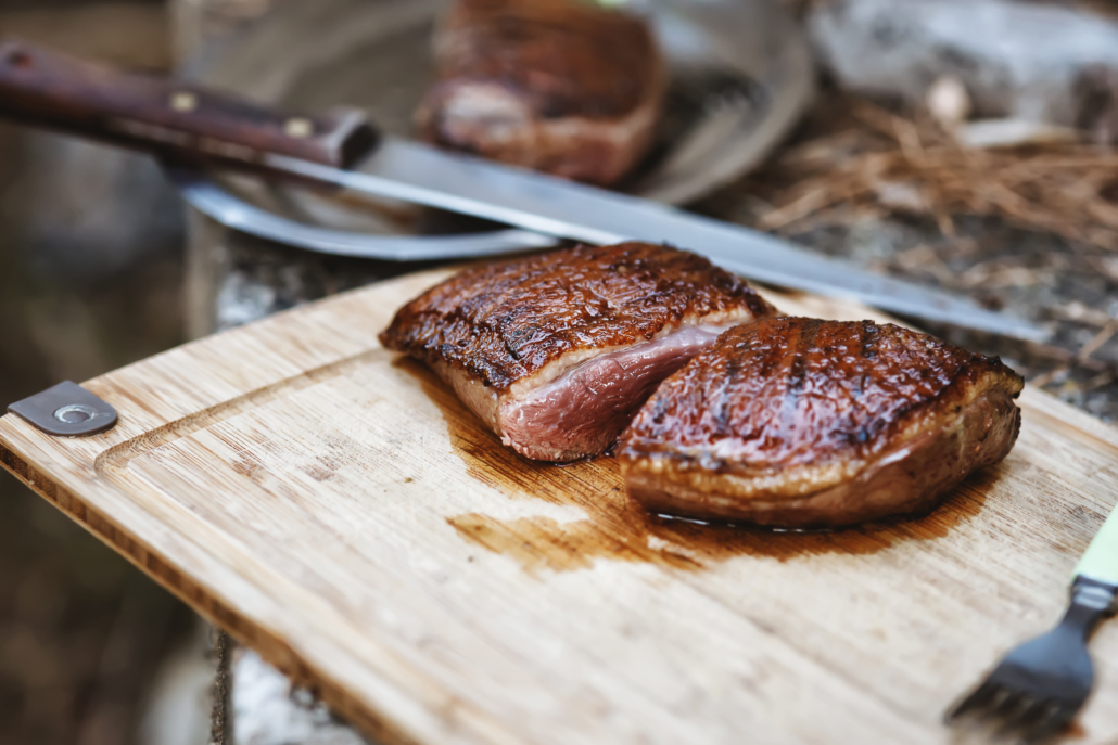 Cut duck steak on the wooden board with a knife in the background