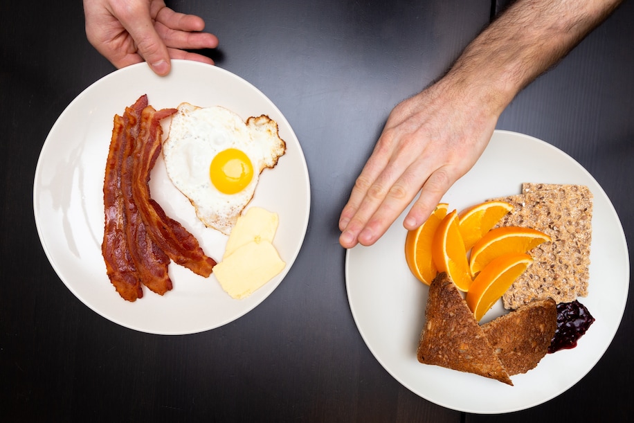 hand reaching for eggs and bacon and hand pushing away fruit and bread
