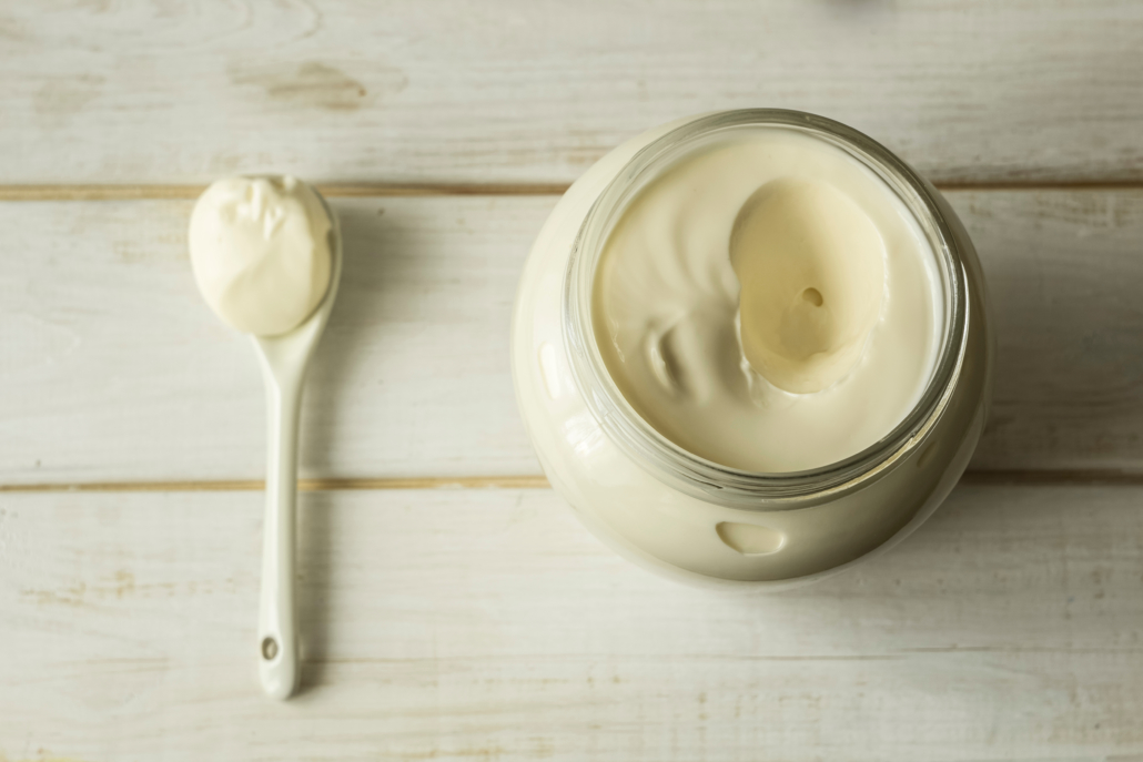 Mayonnaise in a glass jar with a spoon on white wooden boards.