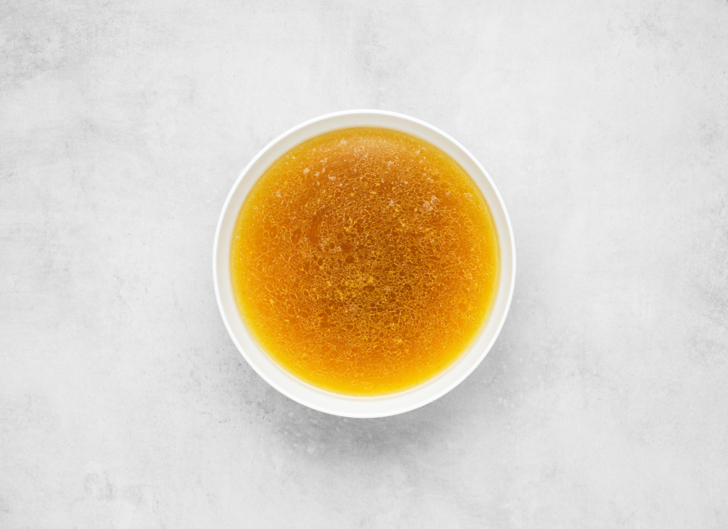 Bone bouillon in white bowl, beef broth on gray concrete background, top view, flat lay, minimalism