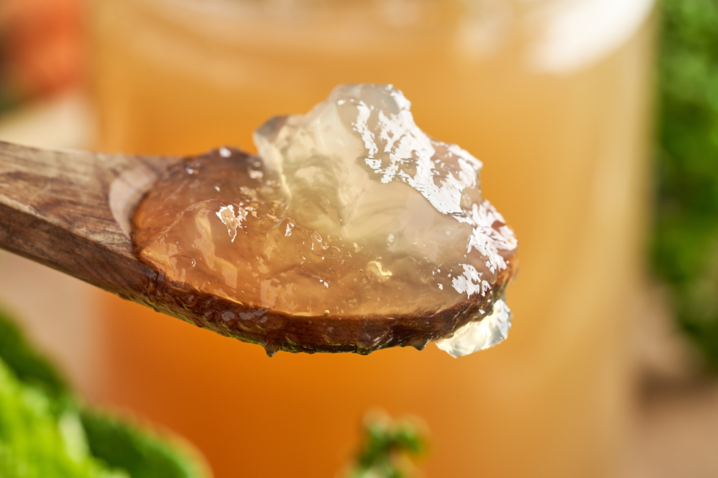 Chilled jellied beef bone broth on a spoon, with a glass jar ful