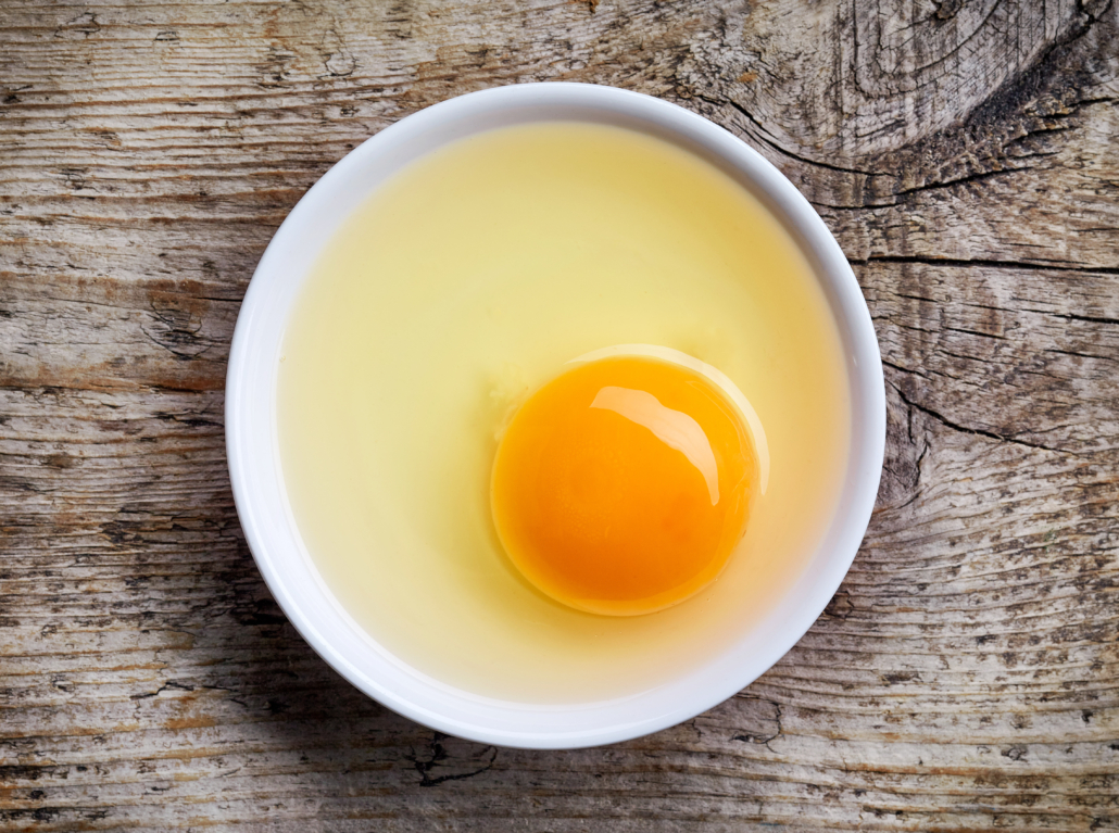 Egg yolk in white bowl on wooden table, top view