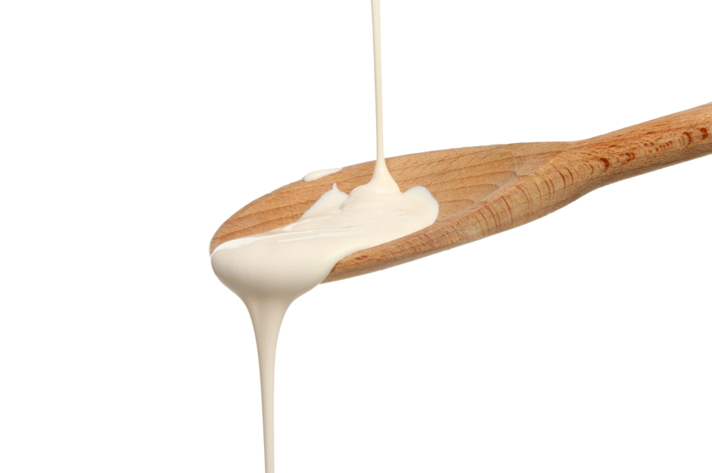 Cream pouring onto a wooden spoon isolated against white
