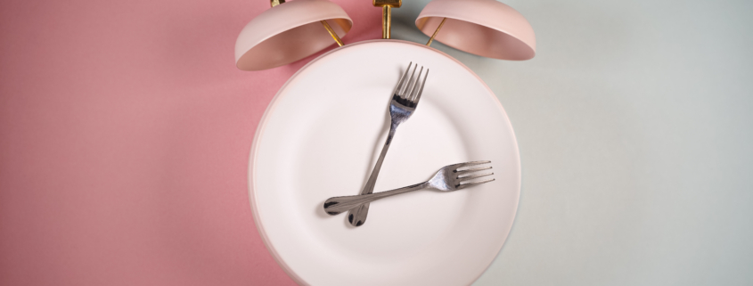 Alarm clock and a plate with fork and knife. Time to eat, diet or Intermittent Fasting concept.