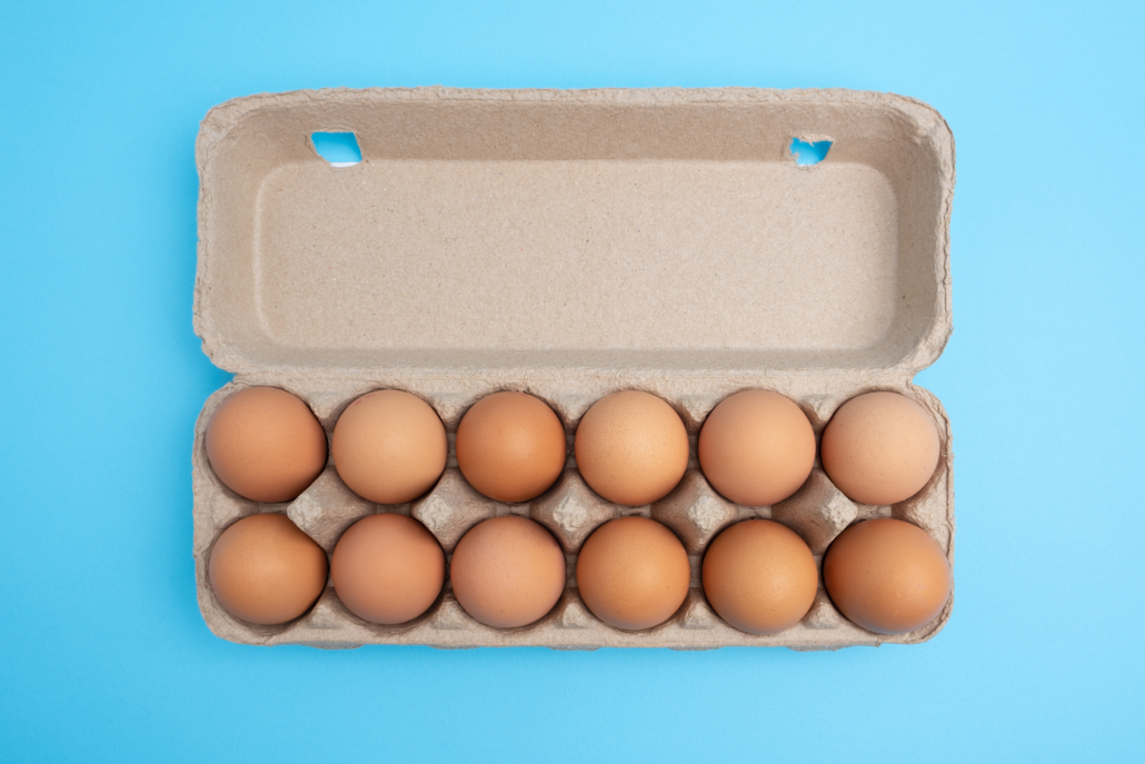 Dozen eggs in open carton on blue background. Top view with copy space