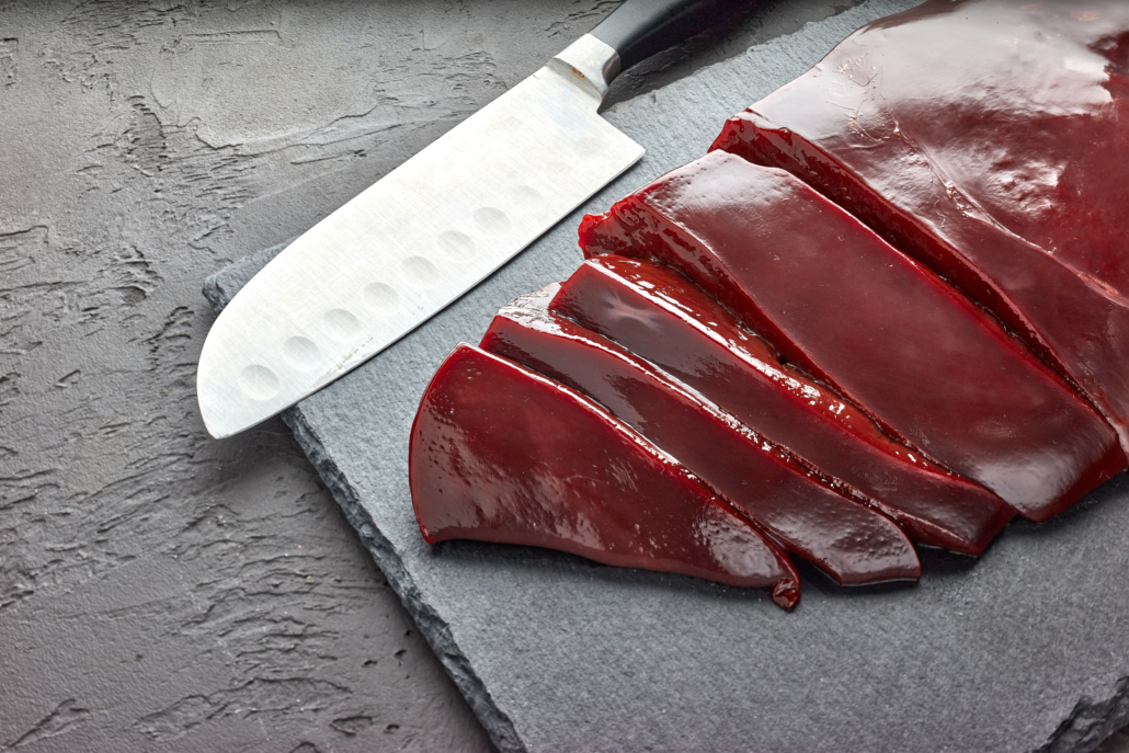 Raw beef livers on a black stone cutting board on dark background. Top view