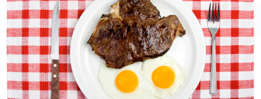 A place setting with a plate of two sunny-side up eggs and a T-bone steak.