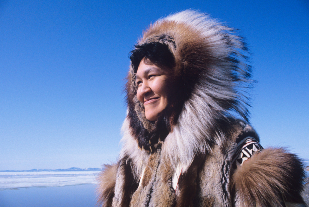 Smiling Eskimo woman wearing traditional clothing in wind against clear blue sky