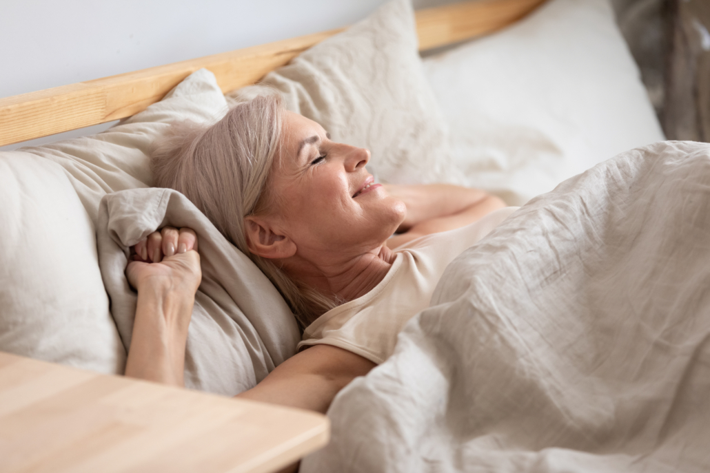 Middle-aged attractive woman lying in bed on comfortable memory foam pillow fresh beige color bed clothes enjoying early morning awakened at home closed eyes dreaming visualizing perfect day concept