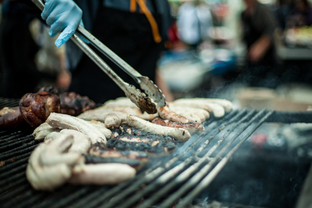 Closeup view with shallow depth of field on hands of a chef using tongs to prepare and grill sausages at a street food stall during farmers market.