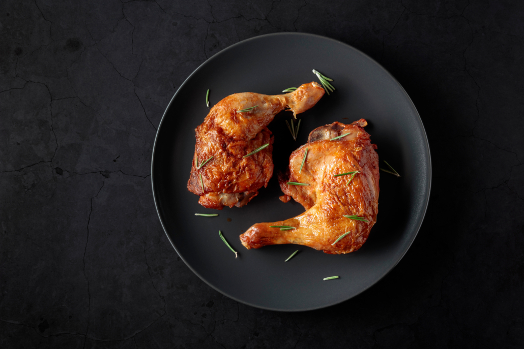 Grilled chicken leg sprinkled with rosemary on a black stone table. Top view with copy space.