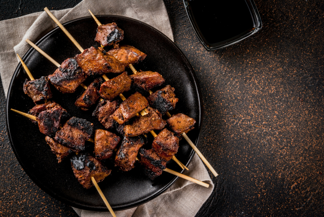 Grilled beef liver on skewers, with teriyaki or soy sauce, yakitori, dark rusty table copy space top view