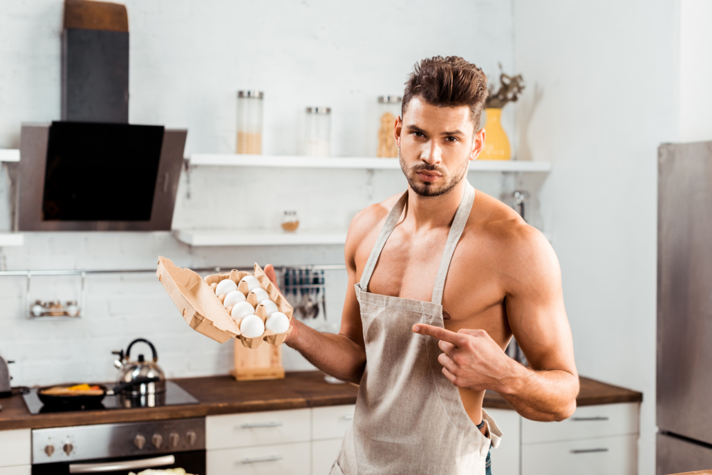 sexy bare-chested man in apron pointing with finger at egg carton