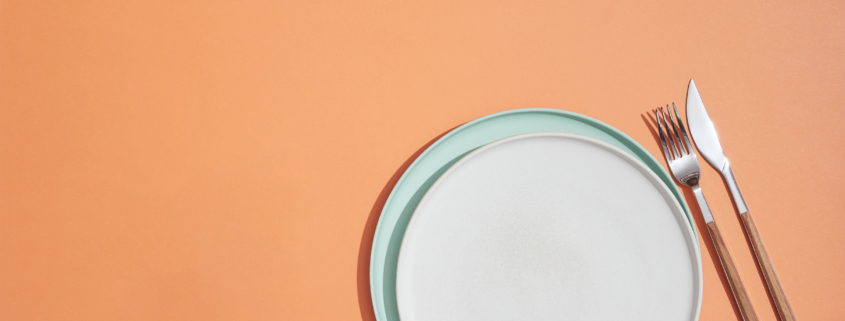 Empty plate and cutlery on orange background, view from above with copy space.