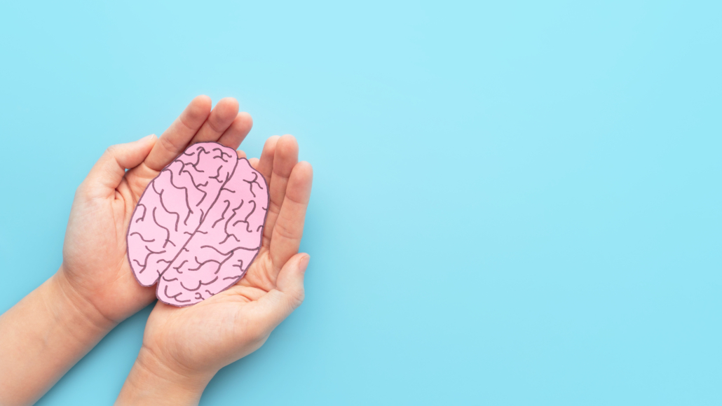 Woman hands holding human brain shape made from paper on light blue background. Awareness of Alzheimer, Parkinson's disease, dementia, stroke, seizure or mental health. Neurology and Psychology care.