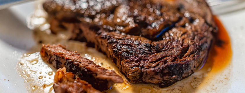 Closeup of knife slicing cutting cooked medium rare well done grilled grass-fed ribeye rib eye meat beef steak on white plate